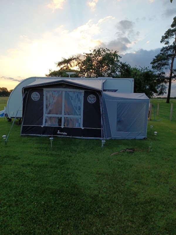 Caravan with a black awning set on green grass, surrounded by trees and a colorful sunset sky.