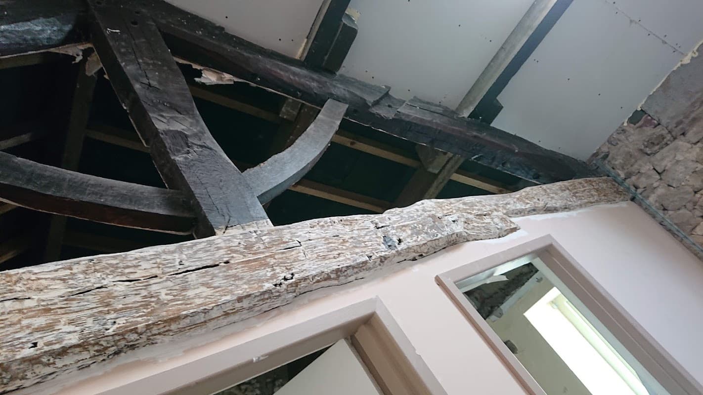 Exposed wooden beams and rustic stone walls in a building under renovation, showcasing historical architectural features.