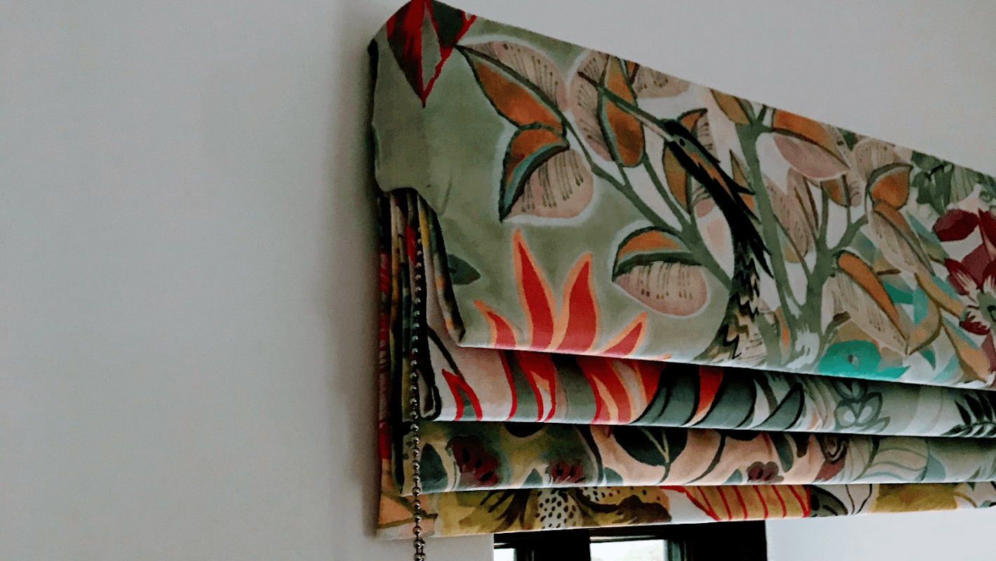 Colorful patterned Roman shades hanging above a window, showcasing floral and botanical designs.