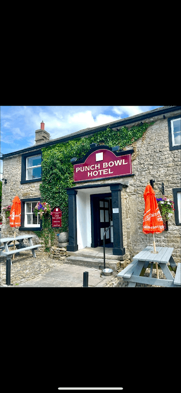 Historic stone building with a sign reading "Punch Bowl Hotel," surrounded by greenery and outdoor seating.
