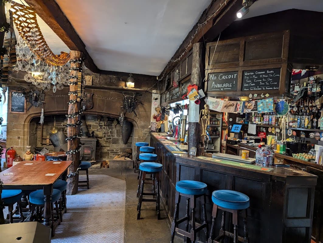 Rustic bar interior with wooden beams, a stone fireplace, colorful stools, and shelves stocked with various drinks.
