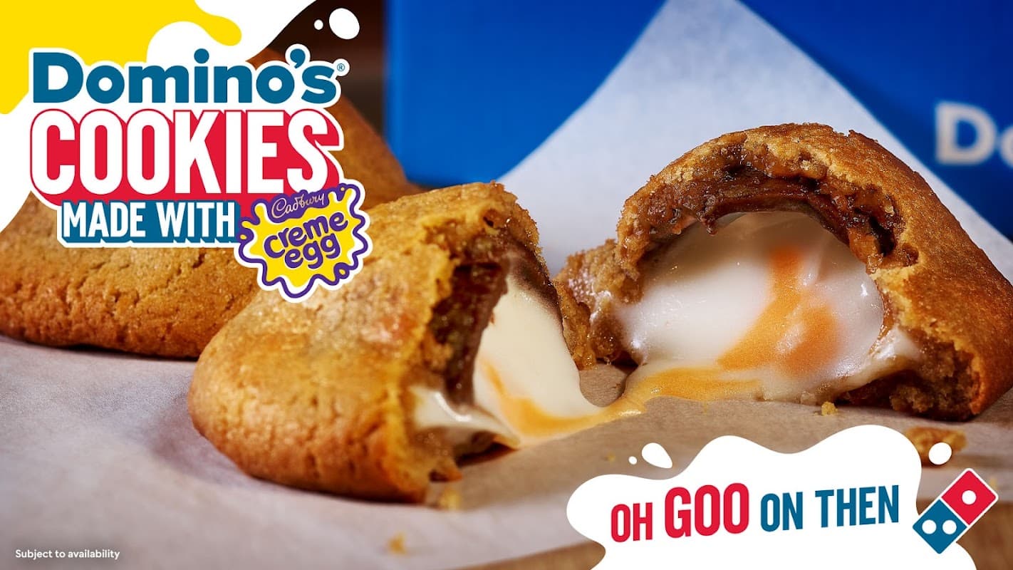 Warm cookies with melted filling, featuring Cadbury Creme Egg, placed on parchment paper with Domino's branding.
