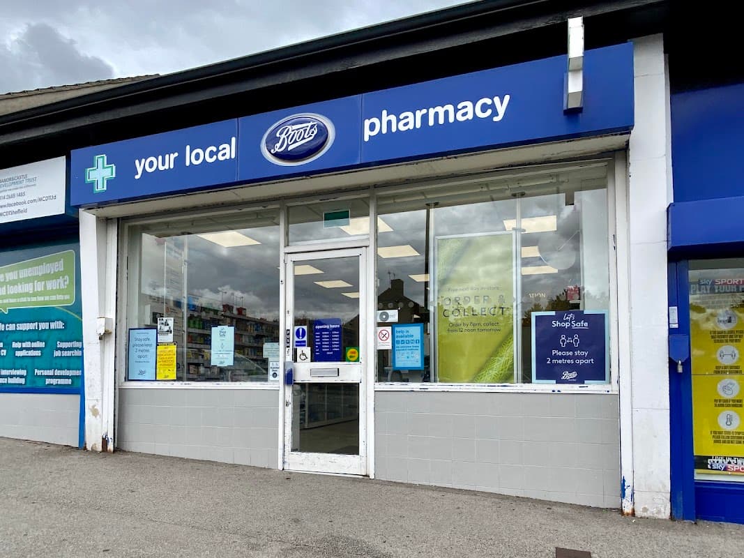 Boots Pharmacy storefront with blue signage, large windows, and various posters displayed outside.