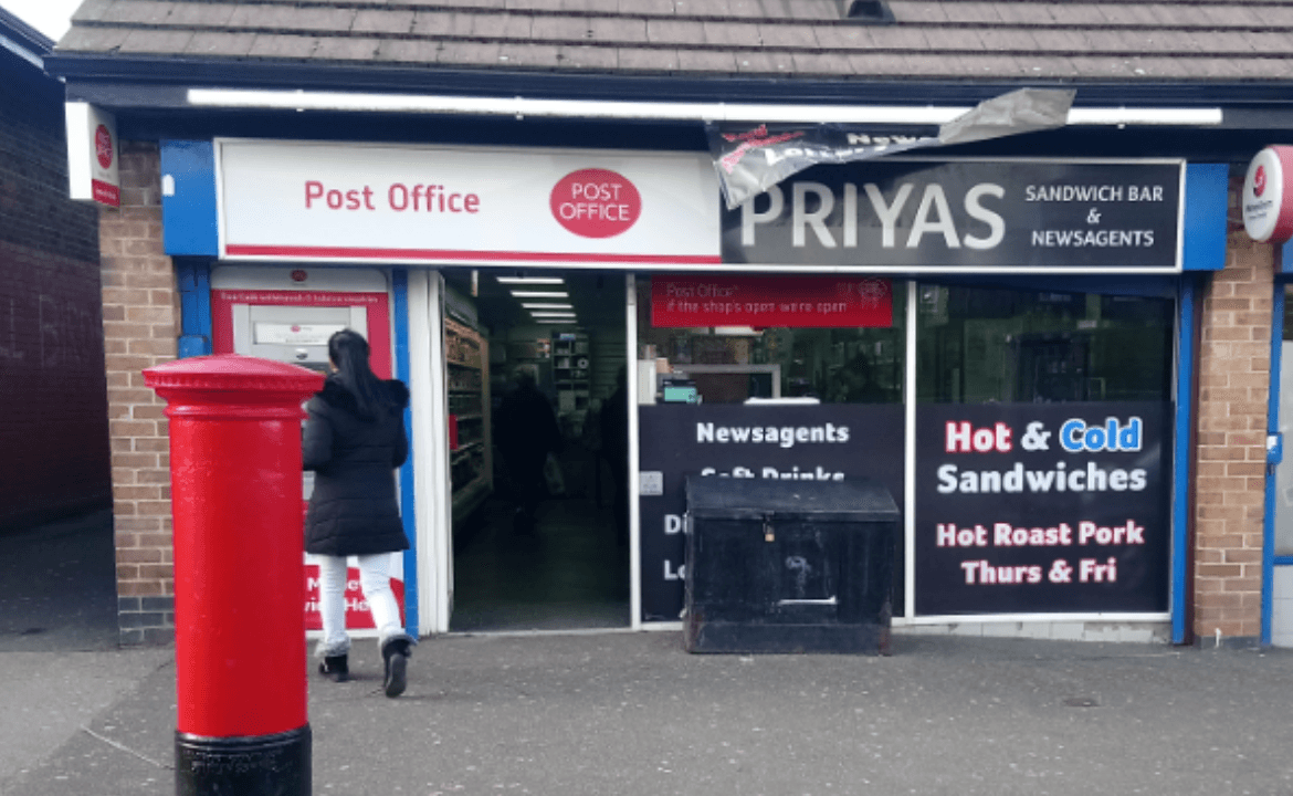 Post Office storefront with red post box, sandwich bar sign, and a customer entering the shop.