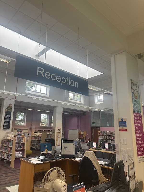 Reception area of Sheffield City Council First Point - Manor Library, featuring desks, computers, and bookshelves.