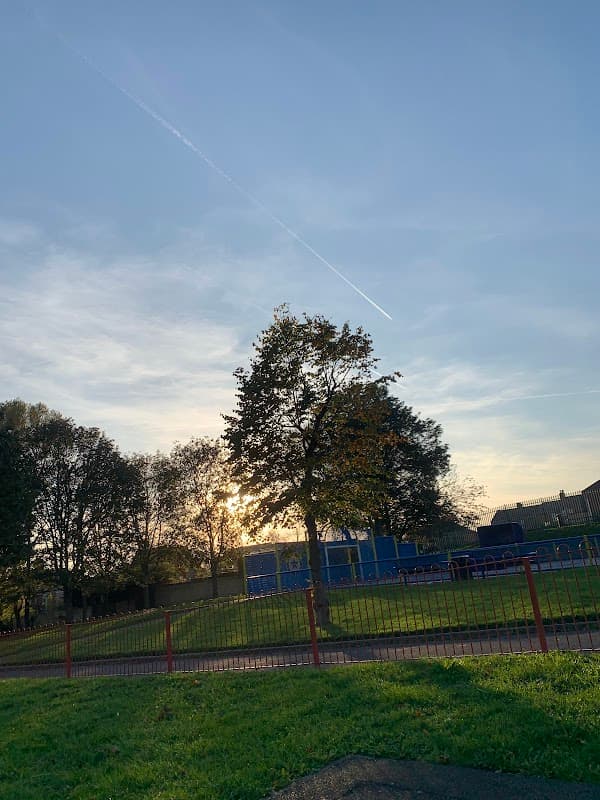 Sunset view over Mapplewell Park, featuring trees, a grassy area, and playground equipment in the background.