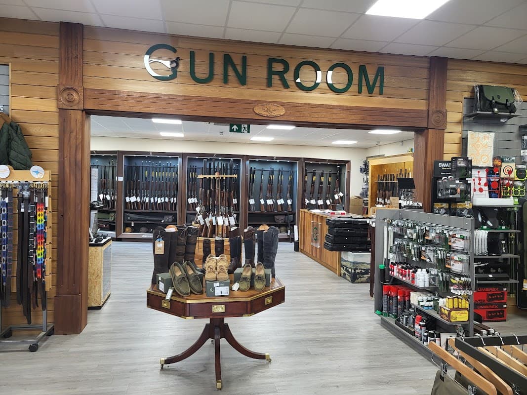 Gun Room display with various firearms, accessories, and footwear in a wooden-paneled shop interior.