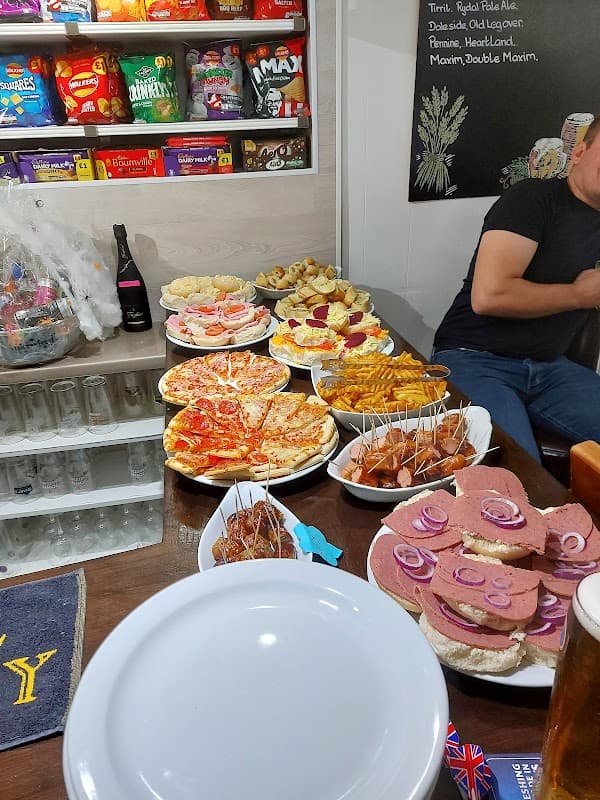 A table filled with various pub snacks, including pizzas, sandwiches, fries, and drinks, in a cozy pub setting.