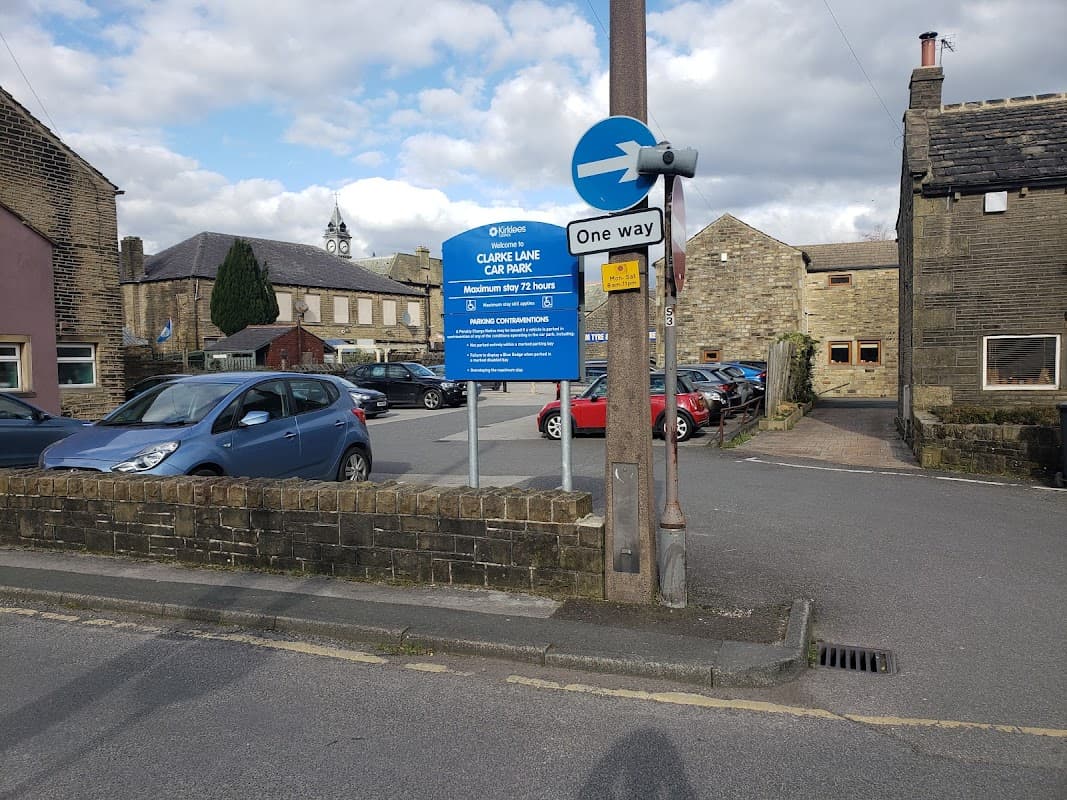Clarke Lane Car Park sign with cars parked, buildings, and a one-way street sign in Meltham, Yorkshire.