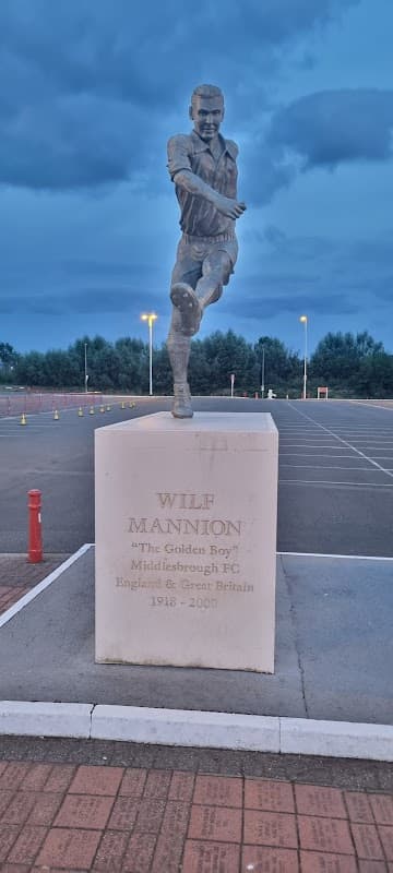 Statue of Wilf Mannion, a footballer, with a cloudy sky and empty car park in the background.