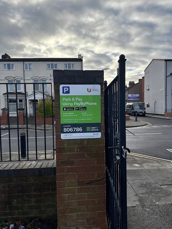 Pay & Display sign for Dartmouth TU car park, with instructions and contact details visible. Cloudy sky in the background.
