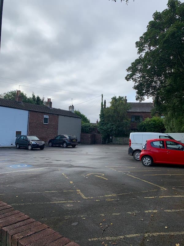 Free parking area with several cars, surrounded by brick buildings and trees under a cloudy sky.
