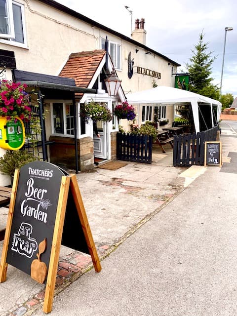 The Black Swan Overton bar entrance with hanging flowers, a beer garden sign, and a canopy outside.