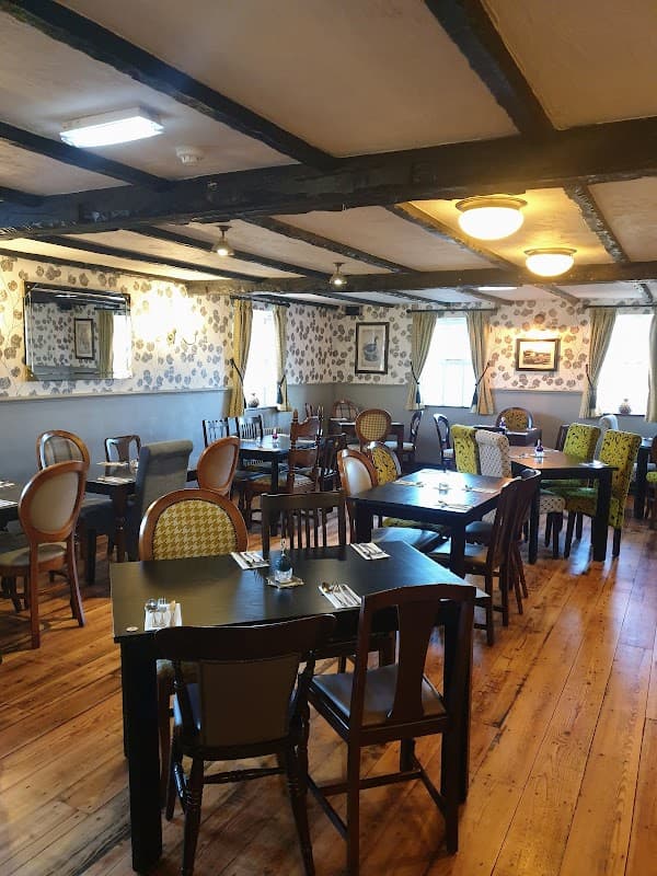 Cozy bar interior with wooden floors, tables, and patterned chairs, adorned with floral wallpaper and soft lighting.