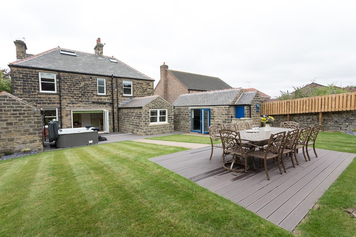 Stone building with a manicured lawn, outdoor dining set, hot tub, and patio area in Millhouse Green, Yorkshire.