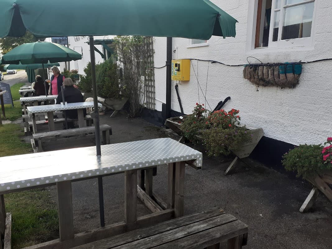 Outdoor seating with wooden tables and green umbrellas, surrounded by potted plants at The Gait Inn in Millington.