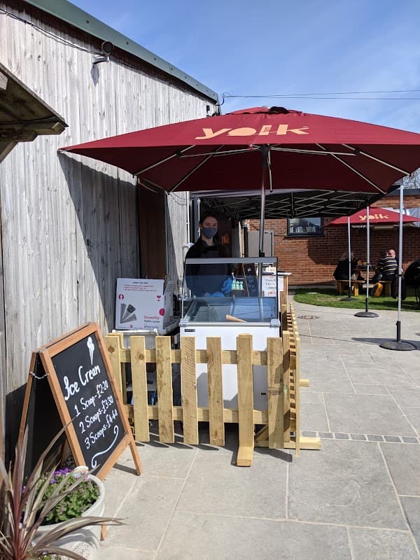 Yolk Farm café with an ice cream stand under an umbrella, wooden fence, and outdoor seating area.