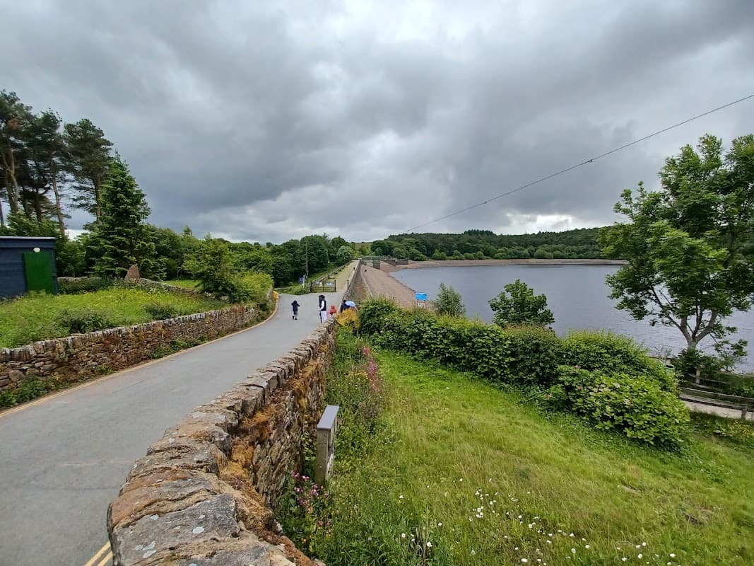 Scenic view of Ogden Water with a dam, pathway, lush greenery, and cloudy sky in Mixenden, Yorkshire.