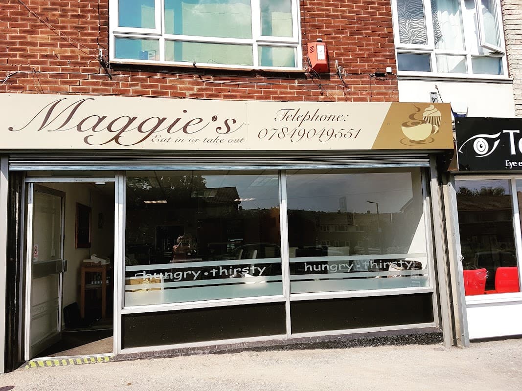 Maggie's Grocers storefront with large windows, signage, and a nearby shop featuring red chairs.