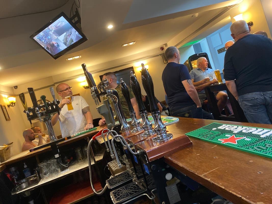 Bar scene at George & Dragon, featuring patrons, beer taps, and a TV screen in a cozy atmosphere.