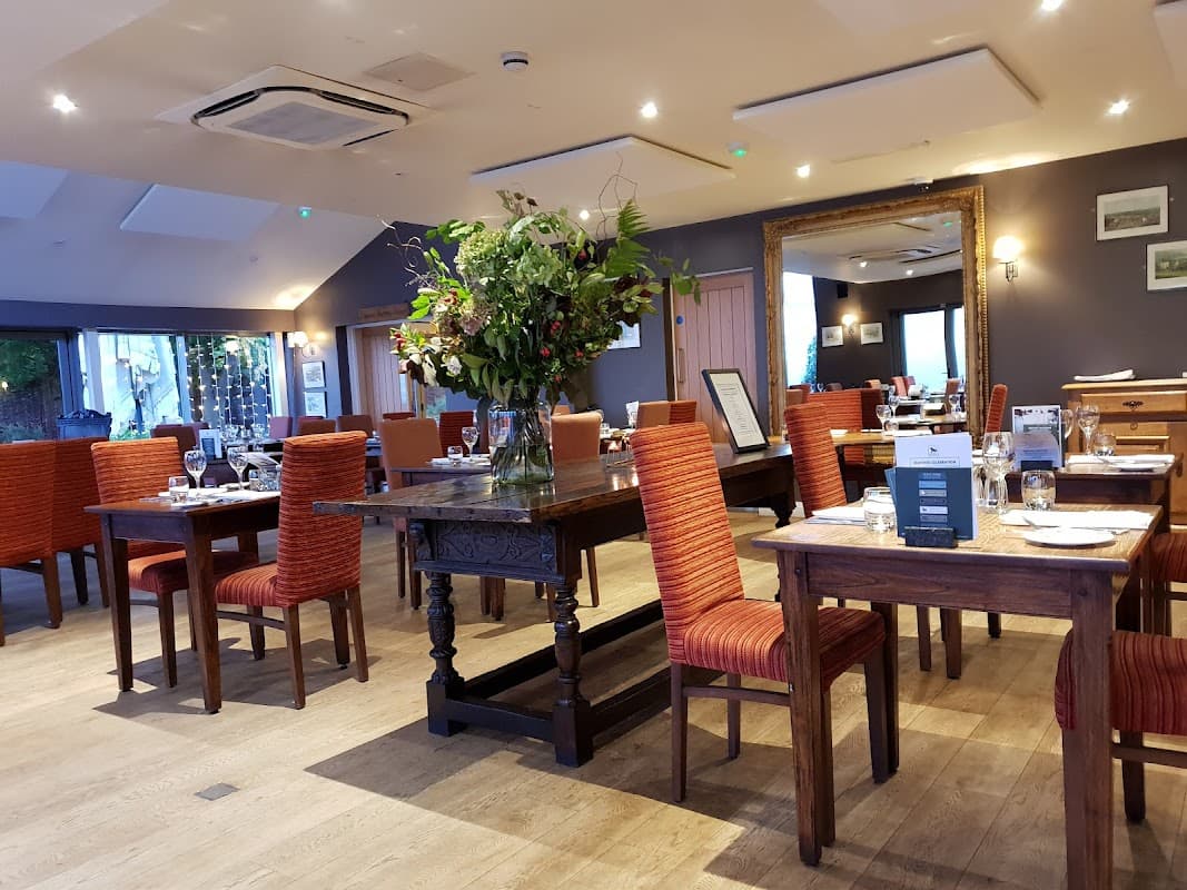 Cozy dining area with wooden tables, orange chairs, and a large floral arrangement in the center. Warm, inviting ambiance.