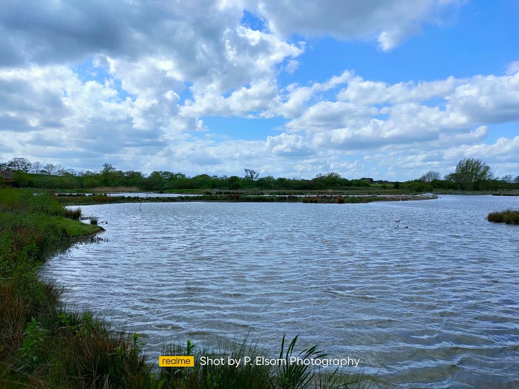 Serene landscape of Filey Dams Nature Reserve with calm waters, lush greenery, and a cloudy sky.