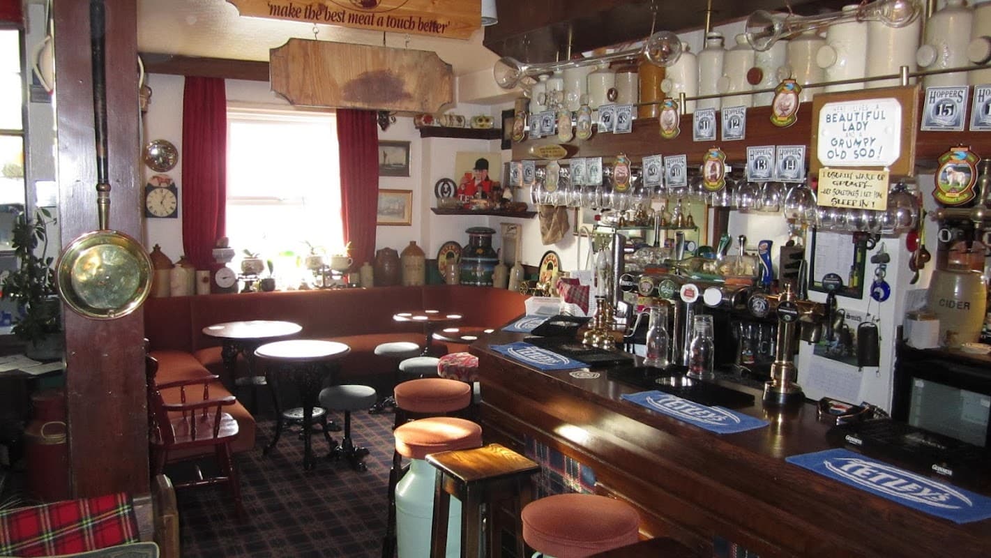 Cozy interior of The Ship Inn featuring wooden bar, stools, glassware, and decorative wall items.