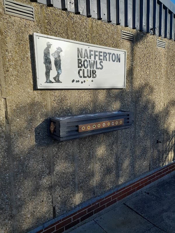 Sign for Nafferton Bowls Club on a textured wall, with a wooden score board beneath it.