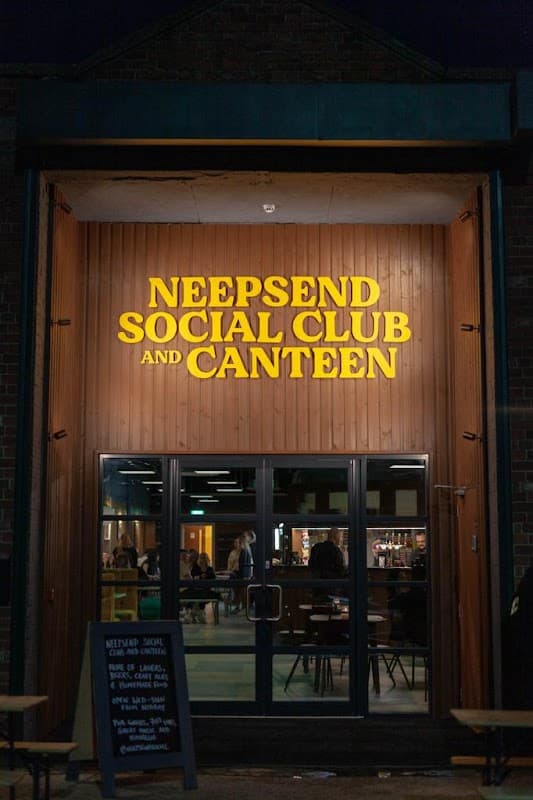 Brightly lit entrance of Neepsend Social Club & Canteen with wooden paneling and a chalkboard sign outside.