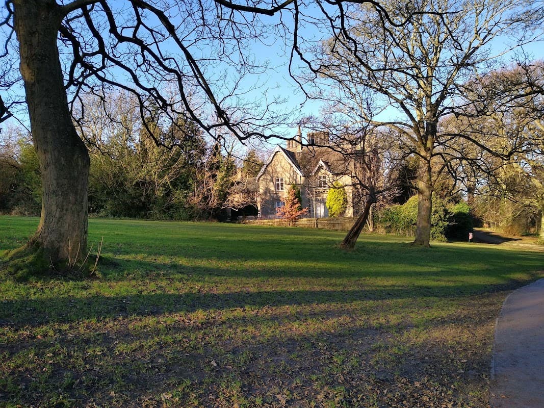 Lush green park with bare trees, a historic stone building, and a winding path under a clear blue sky.