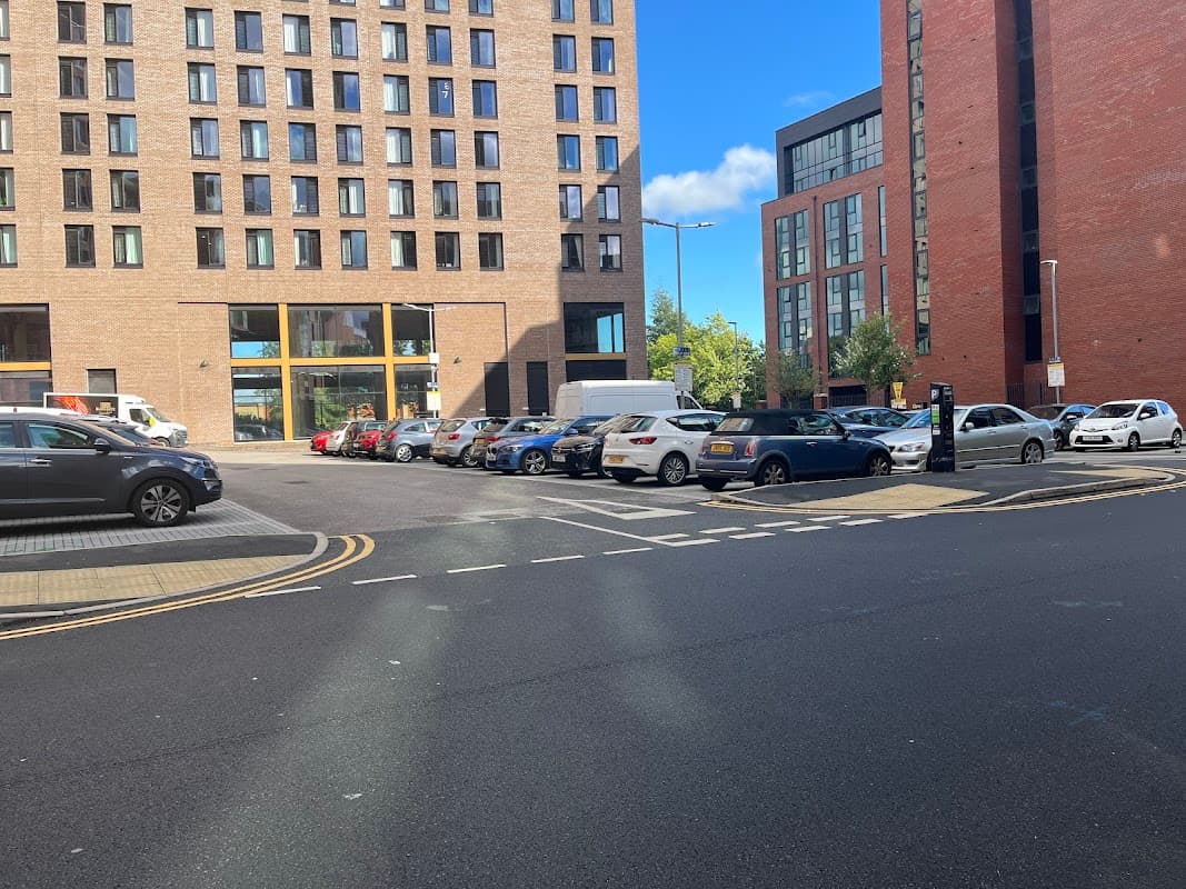 Pay & Display car park with various parked cars, surrounded by modern buildings and a clear blue sky.