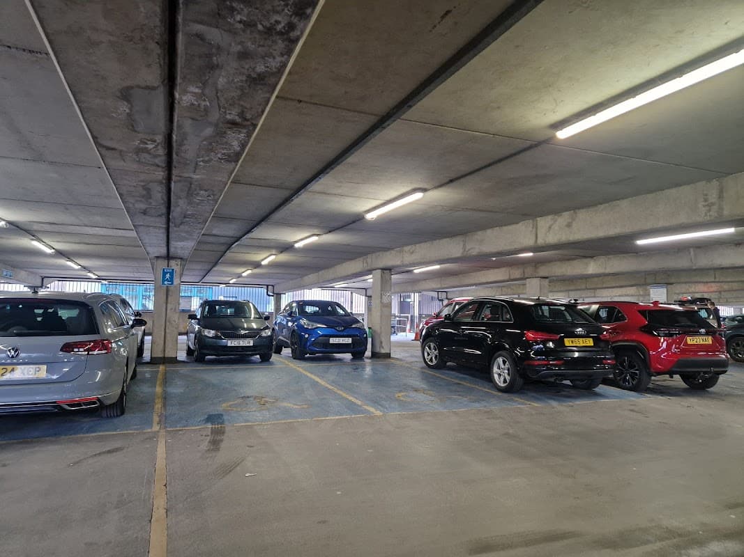 Cars parked in a multi-level car park with concrete walls and bright overhead lights.