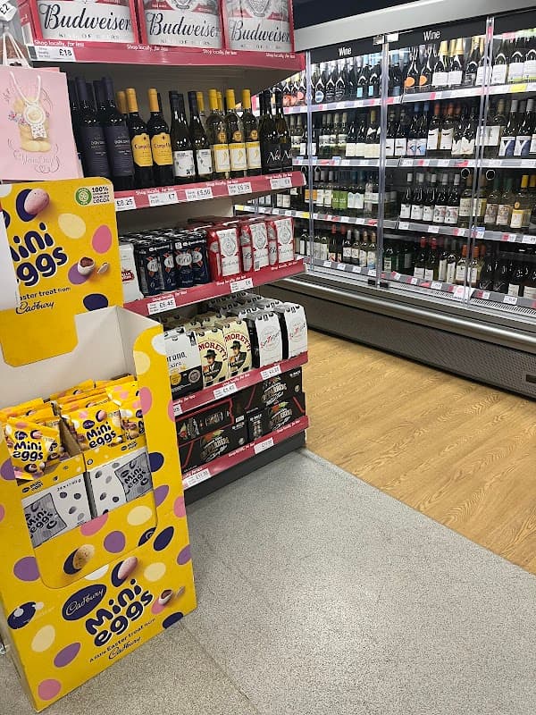 Shelves stocked with wine and beer, featuring a display of Cadbury mini eggs in a corner shop setting.