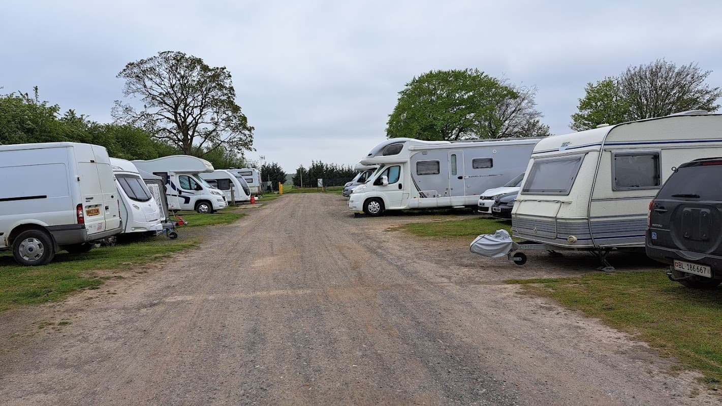 Caravan park with parked RVs and campers along a gravel path, surrounded by greenery and trees in Newthorpe.