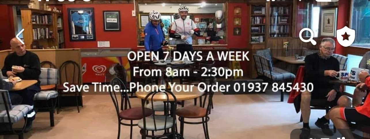 Interior of The Great British Diner with customers, cyclists, and a sign displaying opening hours and contact info.