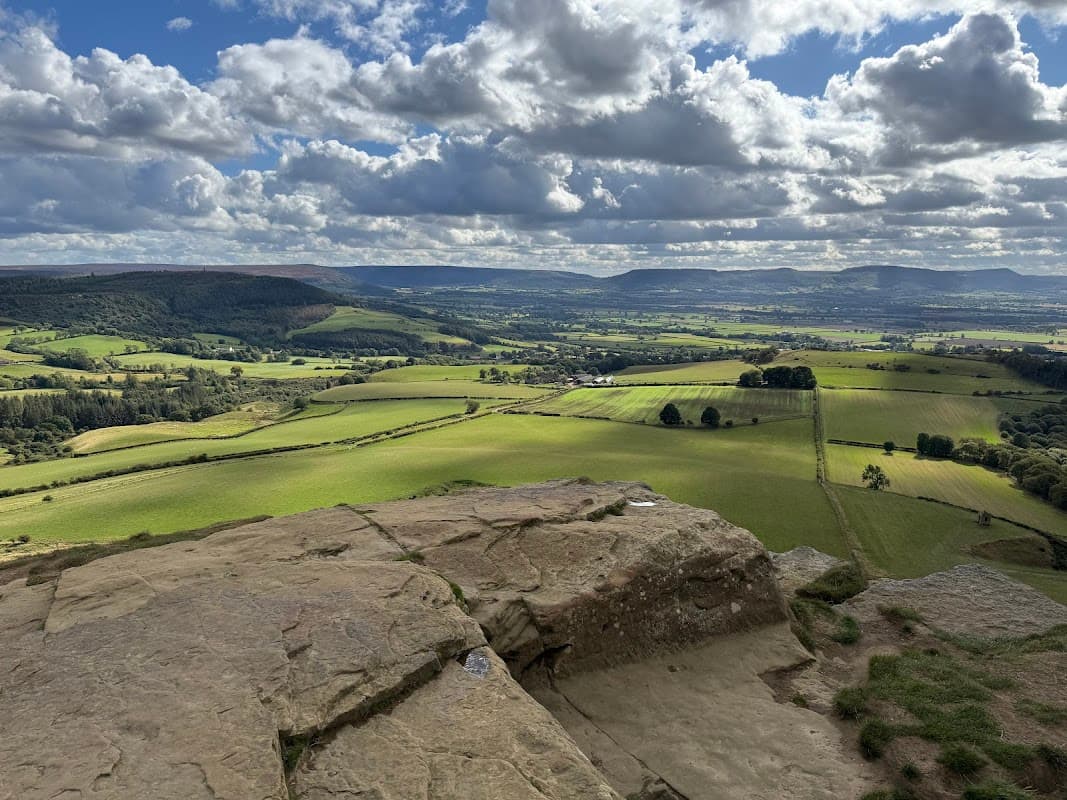 Vast green fields and rolling hills under a partly cloudy sky, with distant mountains visible on the horizon.