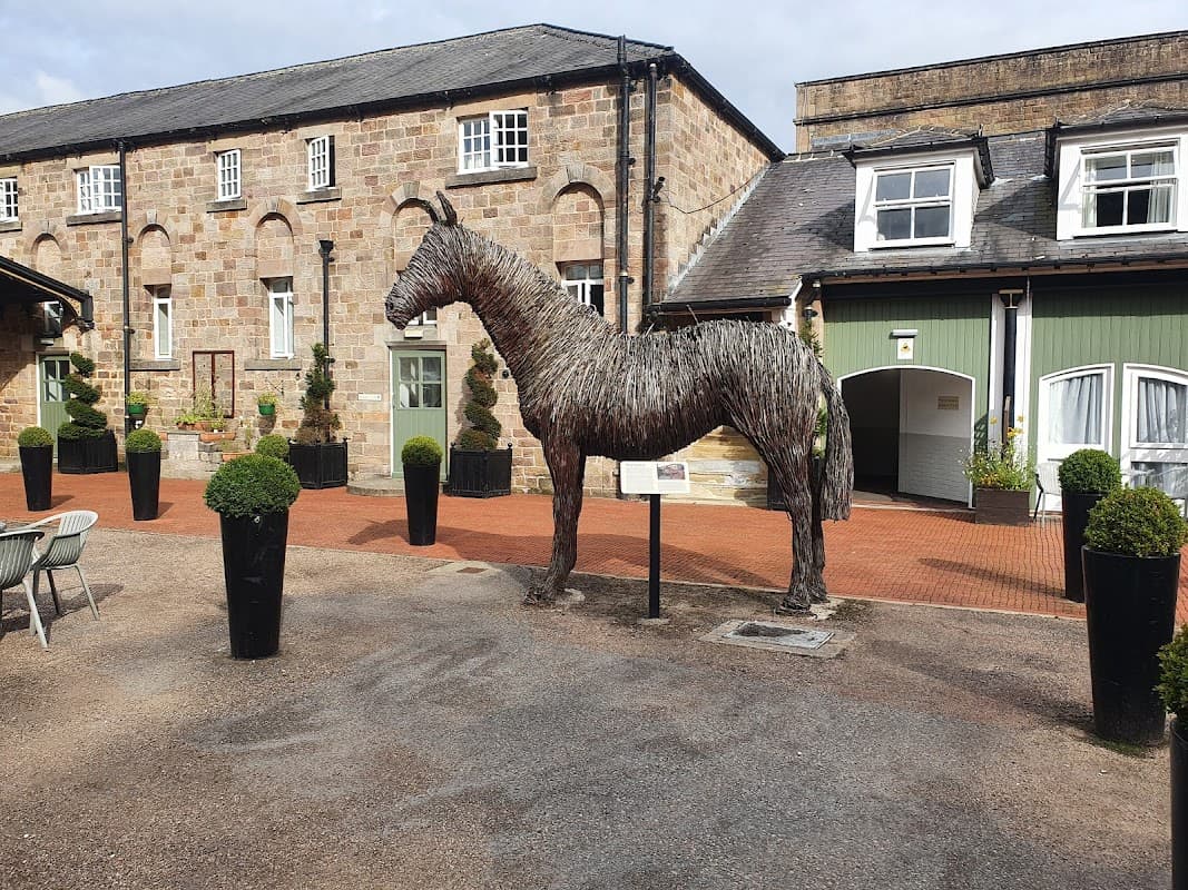 A large straw horse sculpture stands in a courtyard surrounded by potted plants and a brick building.