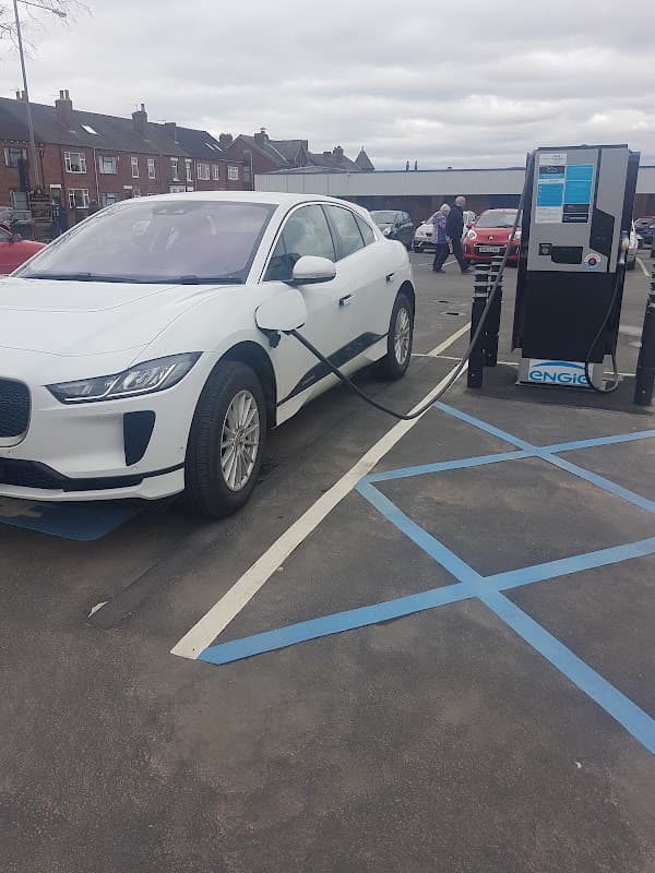 A white electric vehicle charging at a station in West Street Car Park, with buildings visible in the background.