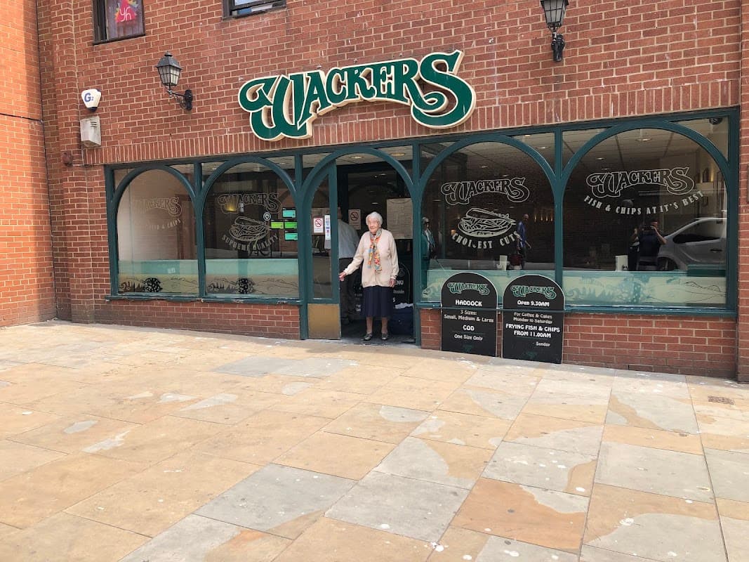 A woman stands at the entrance of a fish and chips shop named "Jackers" in North Cave, Yorkshire, with a brick facade.