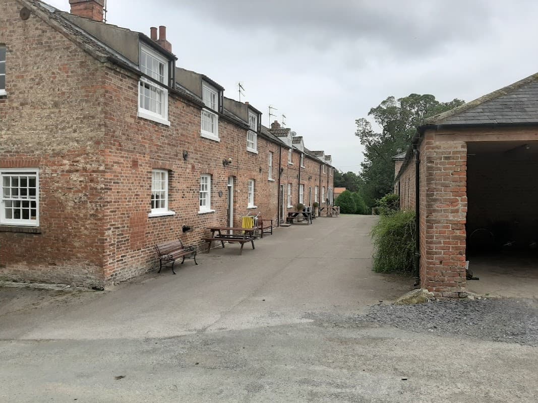 Brick cottages line a gravel path, with benches and greenery in a tranquil rural setting in North Dalton, Yorkshire.