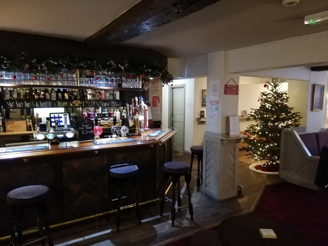 A cozy bar with a wooden counter, stools, festive decorations, and a Christmas tree in the background.