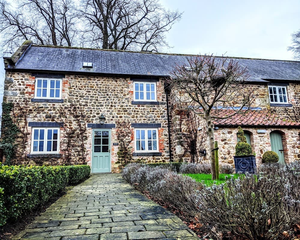 Charming stone hotel with green door, surrounded by trimmed hedges and trees, in a serene Yorkshire setting.
