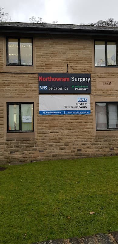Signage for Northowram Surgery featuring NHS contact details and COVID-19 vaccination information on a stone building.