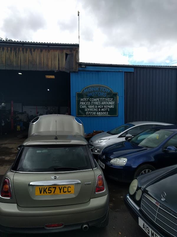 Sign for Monkton Motors on a blue wall, surrounded by parked cars in a garage setting.