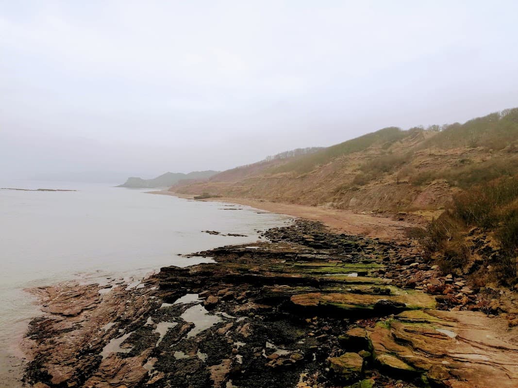 Rocky shoreline with gentle waves, cliffs in the background, and a cloudy sky at Cayton Bay, Scarborough.