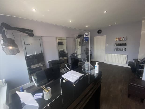 Modern hair studio with styling chairs, mirrors, and a reception desk featuring health safety signage.