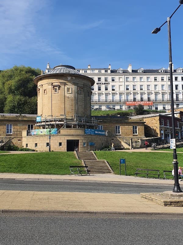 Historic building with a round tower, scaffolding, and green lawns, set against a blue sky in Osgodby, Scarborough.