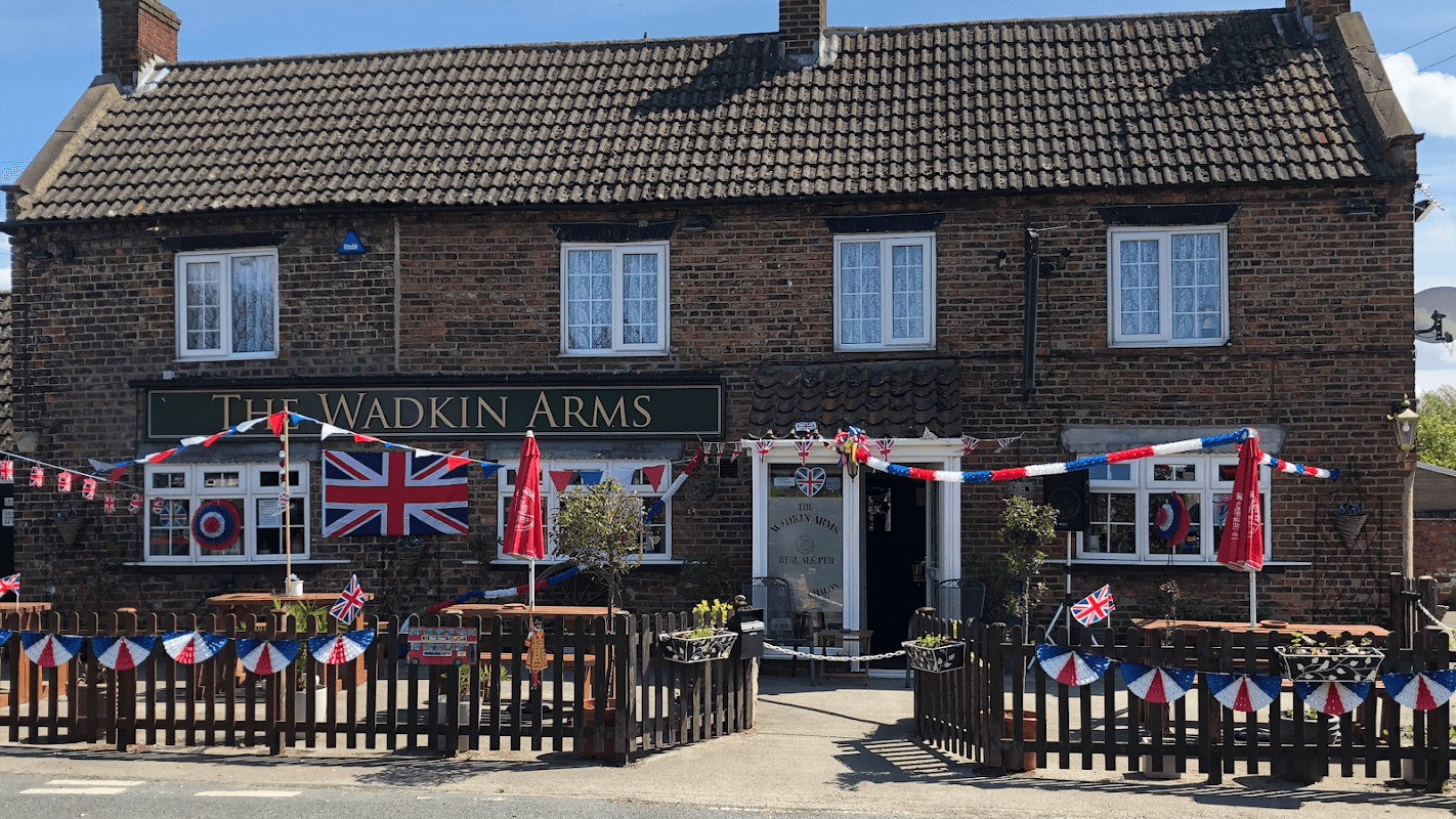 The Wadkin Arms pub adorned with Union Jack flags and bunting, featuring outdoor seating and a welcoming entrance.
