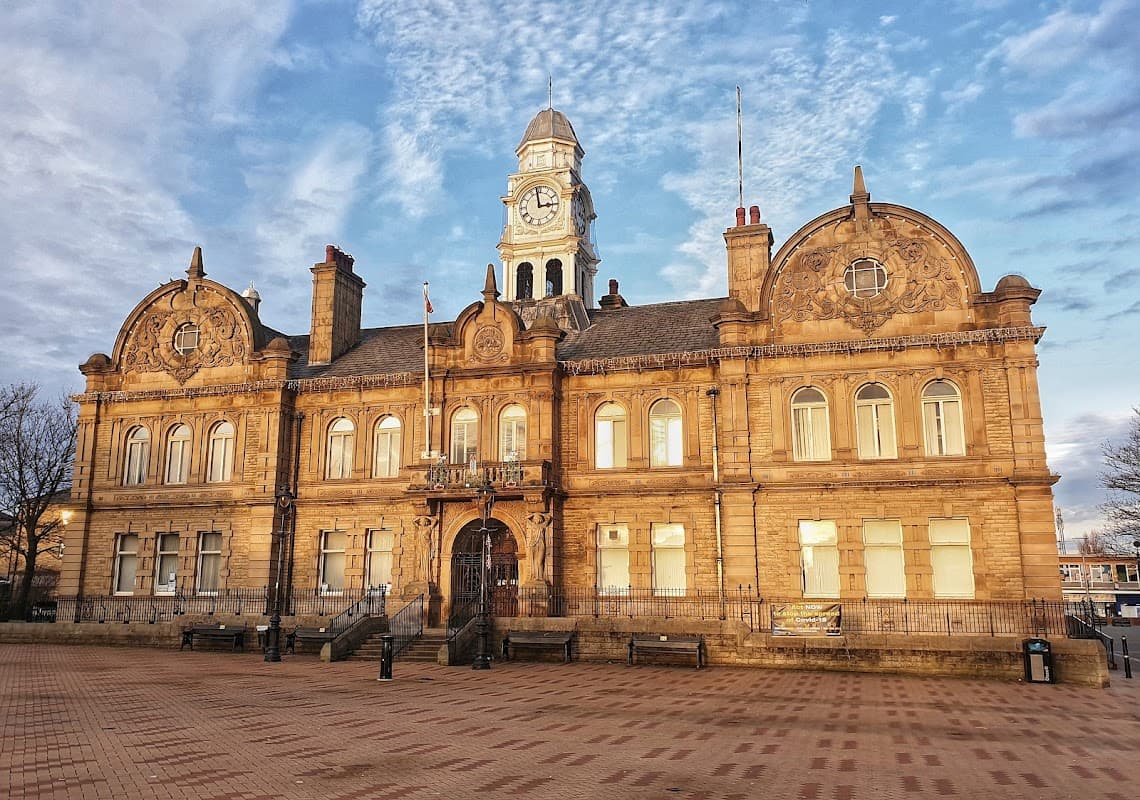 Victorian-style town hall with a clock tower, intricate stonework, and a blue sky backdrop in Ossett, Yorkshire.
