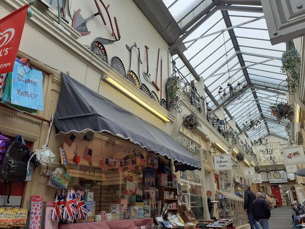 Victorian-style arcade with shops, decorative fans on walls, and a glass roof, bustling with shoppers.